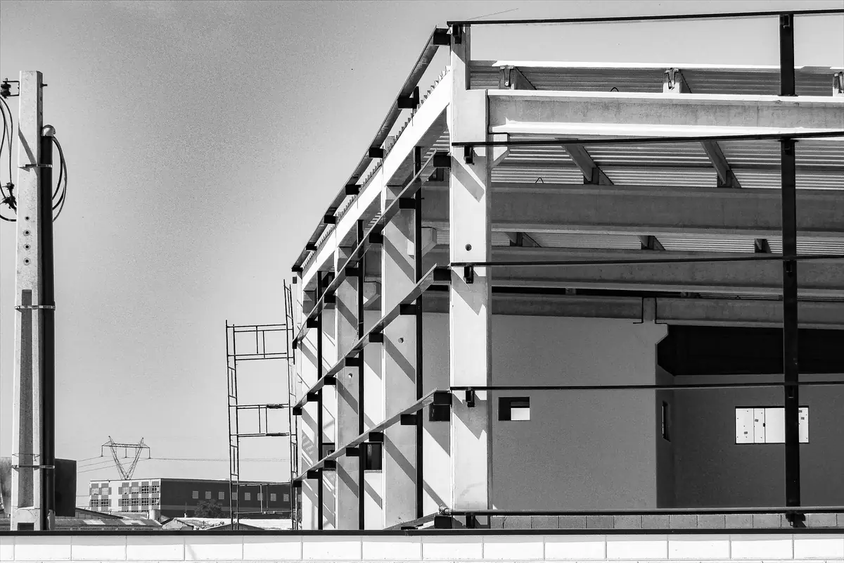 Edificação com estrutura metálica aparente em fase de montagem, em preto e branco