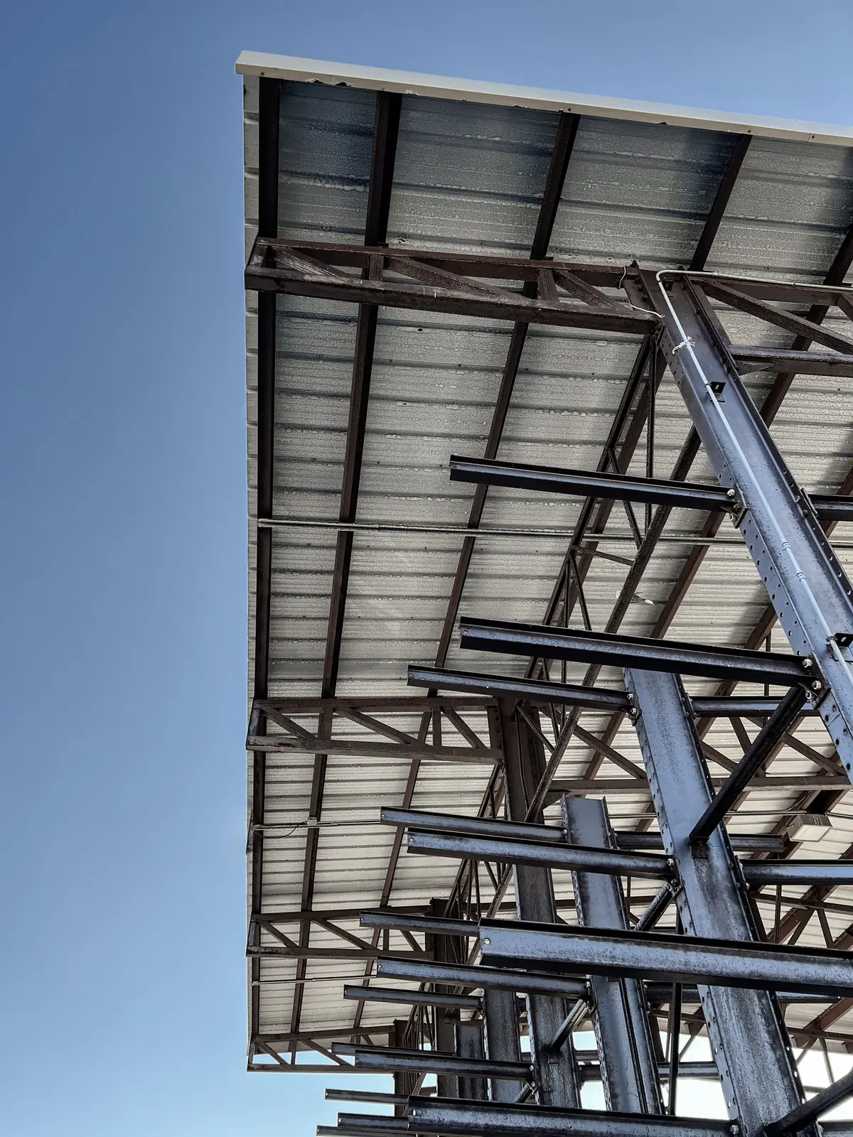 Estrutura metálica de galpão com terças e telhas metálicas vista de baixo, contra o céu azul