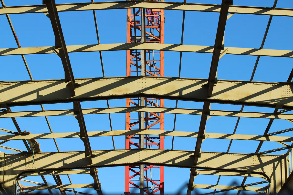 Estrutura metálica de cobertura em montagem com grua ao fundo e céu azul